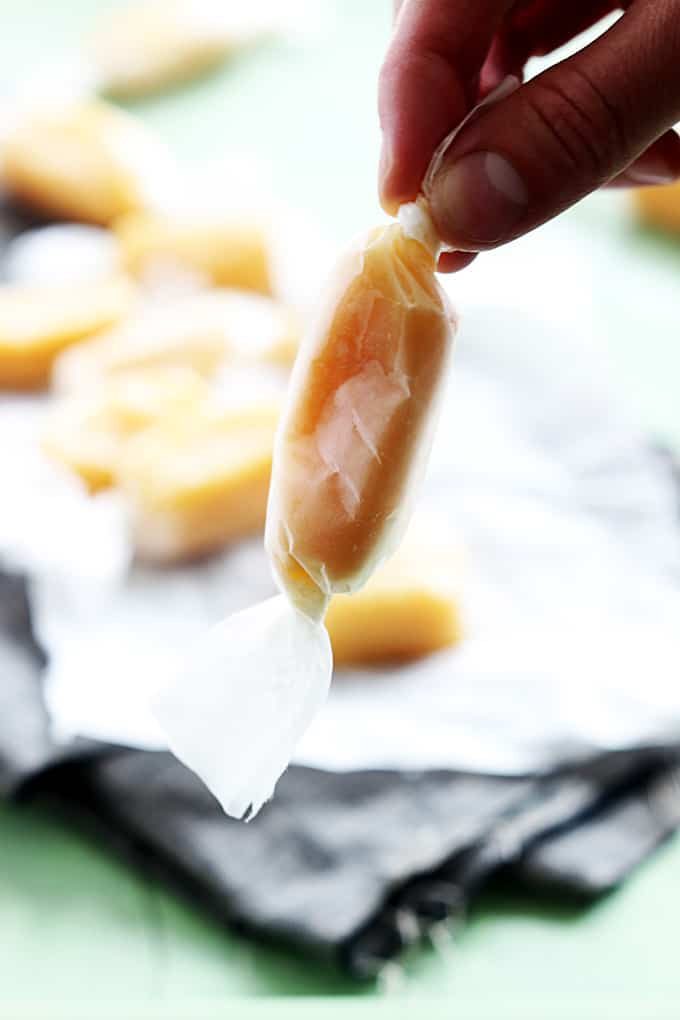 a hand holding a wrapped soft caramels with more caramels faded in the background.