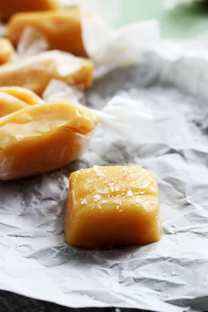 close up of soft caramels individually wrapped with the front one unwrapped and topped with sea salt.