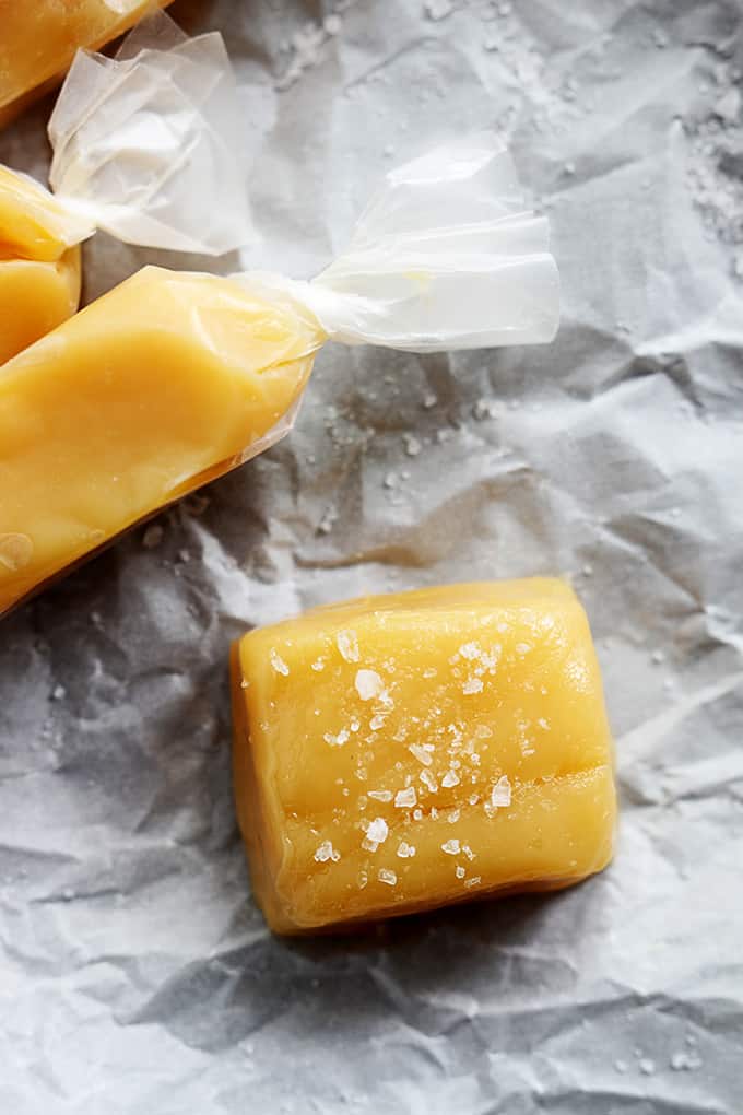 close up top view of individually wrapped soft caramels with the front one unwrapped and topped with sea salt.