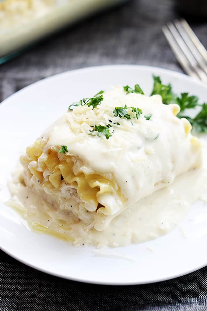 a white chicken lasagna rollup on a plate with a fork on the side.