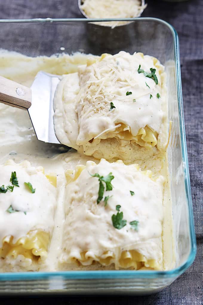 a metal spatula taking a a white chicken lasagna rollup from a tray of rollups.