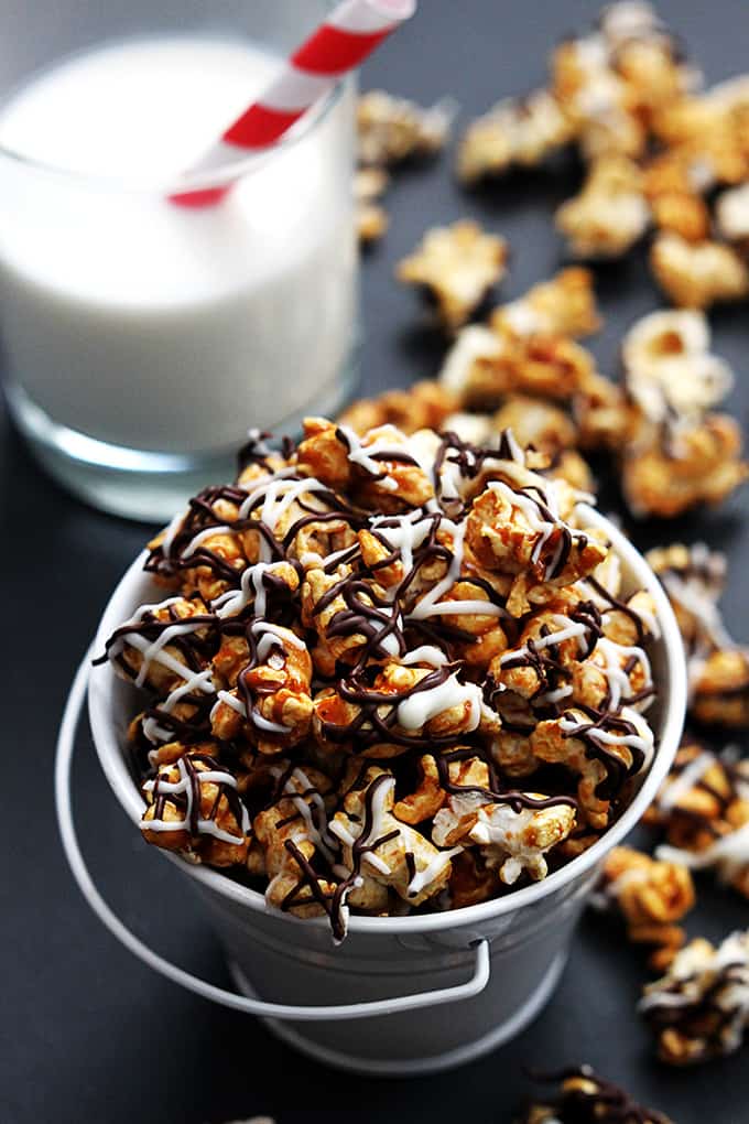 zebra caramel corn in a tin bucket with more popcorn and a glass of milk on the side.