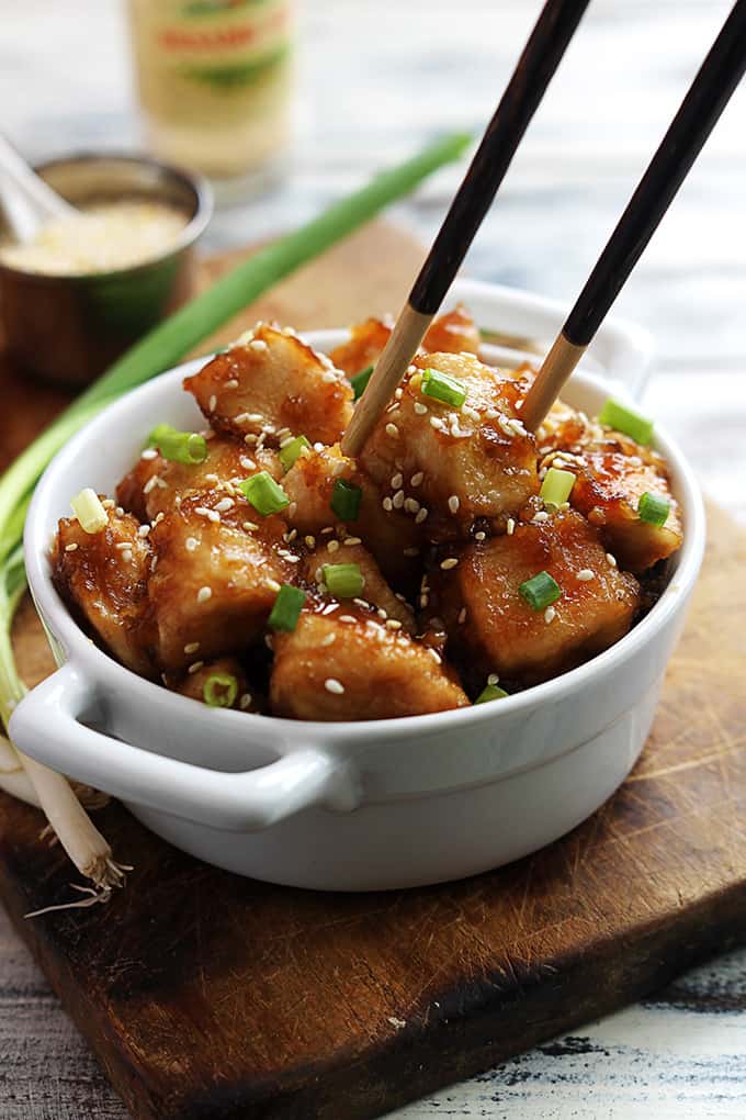 baked sesame chicken in a bowl with chopsticks picking up a piece of chicken.