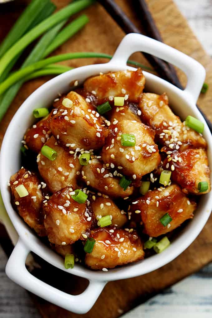 top view of baked sesame chicken in a bowl with green onions on the side.