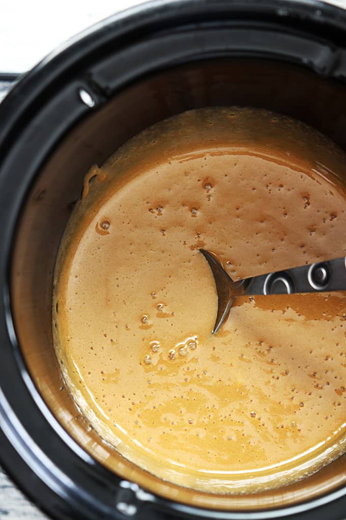 top view of caramel fondue in a slow cooker with a serving spoon.