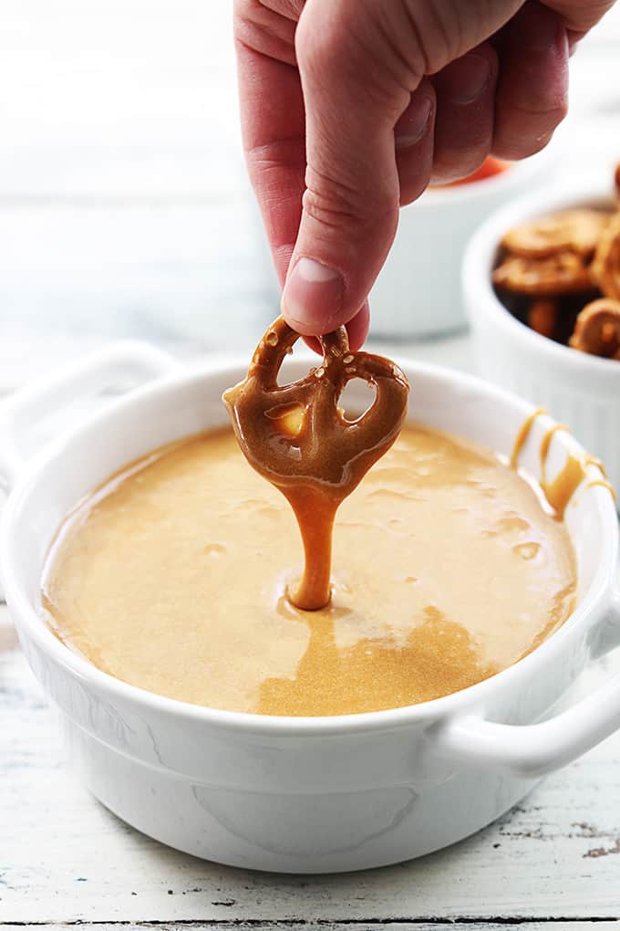 a hand holding a pretzel dipped in caramel fondue above a bowl of fondue.