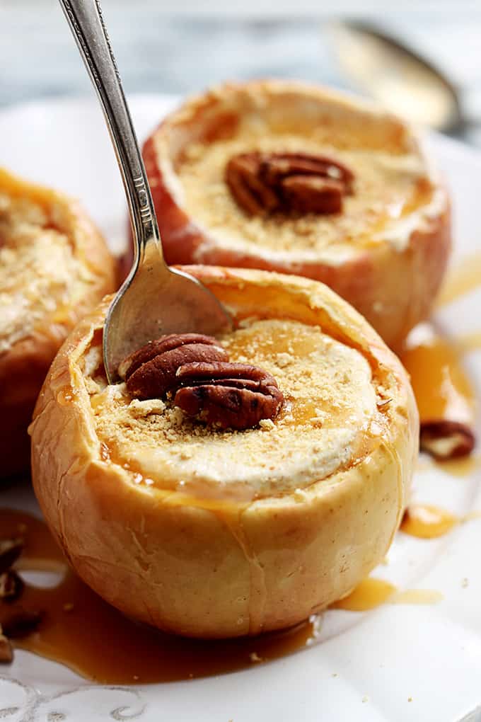 close up of a cheesecake stuffed baked apples with a spoon in it with more apples faded in the background.