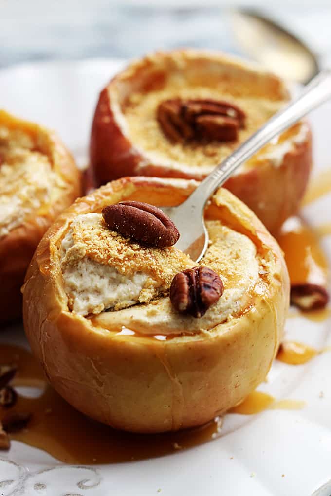 close up of cheesecake stuffed baked apples on a plate with the front apple having a spoon on the top of it.