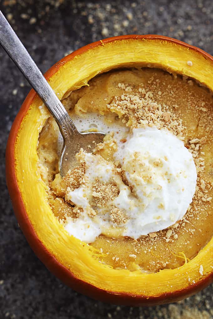 close up top view of a pumpkin cheesecake stuffed pumpkin topped with whipped cream with a spoon.