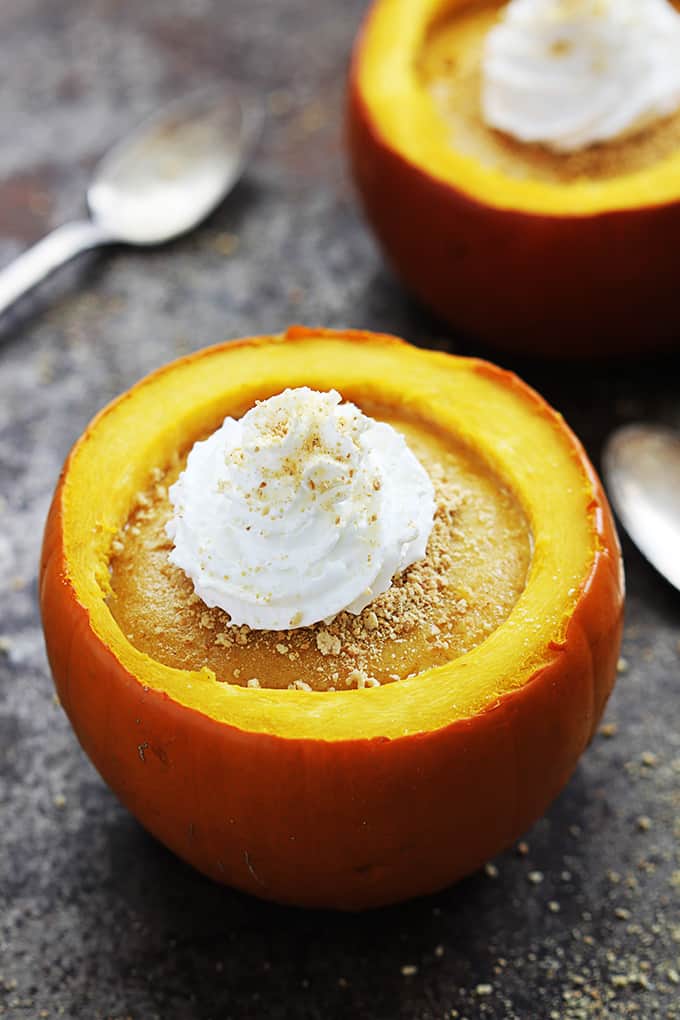 a pumpkin cheesecake stuffed pumpkin topped with whipped cream with spoons and another pumpkin in the background.