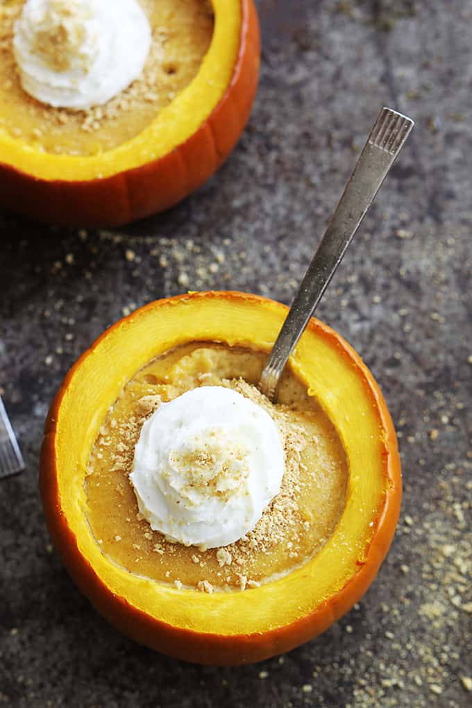 topped view of pumpkin cheesecake stuffed pumpkins topped with whipped cream with a spoon in the front pumpkin.