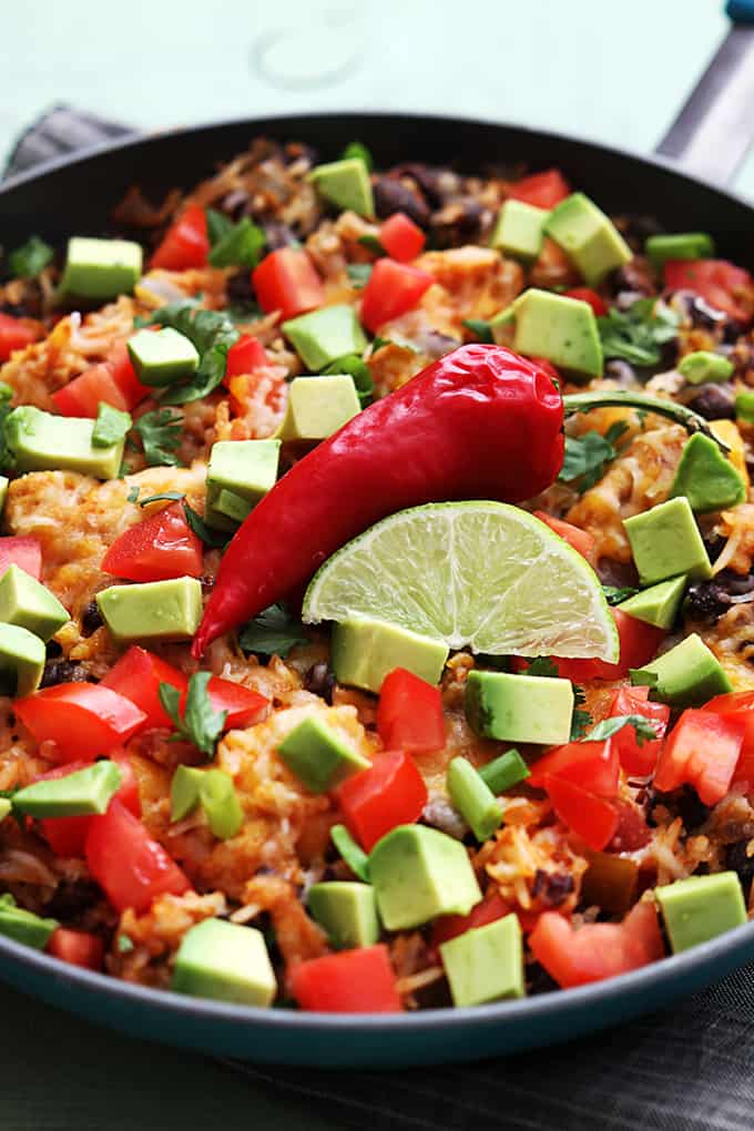 close up of chicken taco rice skillet topped with a red chili pepper and a slice of a lime in a skillet.