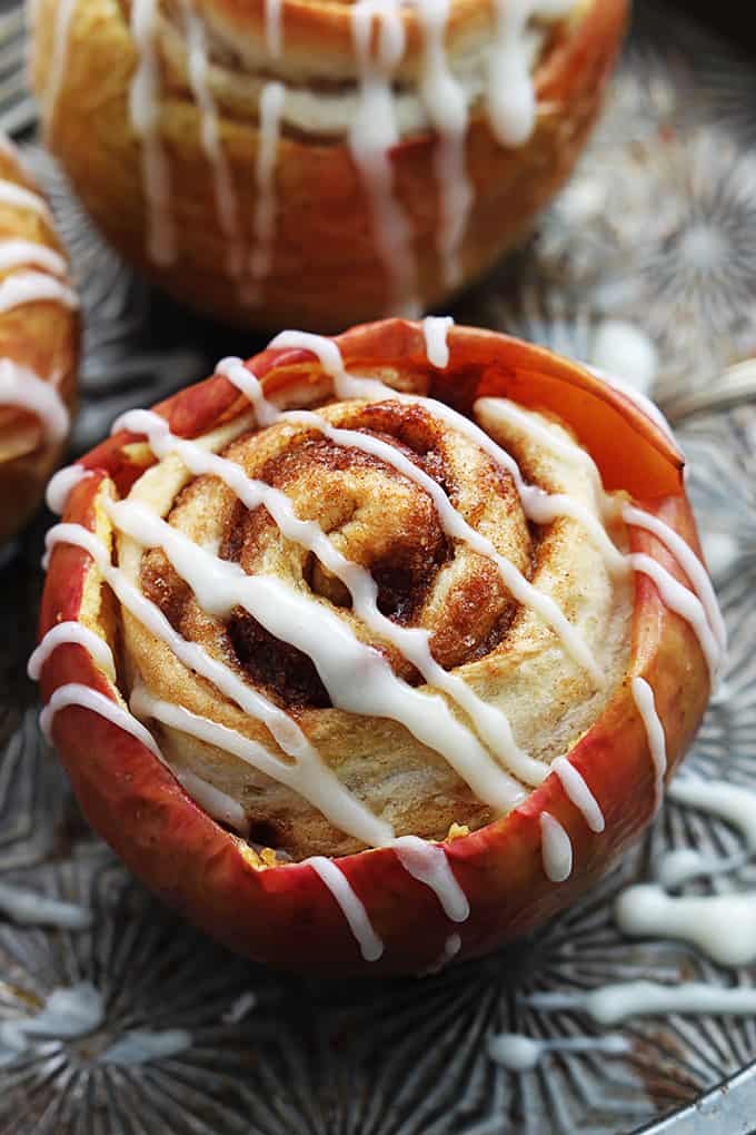 top view of a cinnamon roll stuffed baked apple topped with cream cheese frosting with more stuffed apples on the side.
