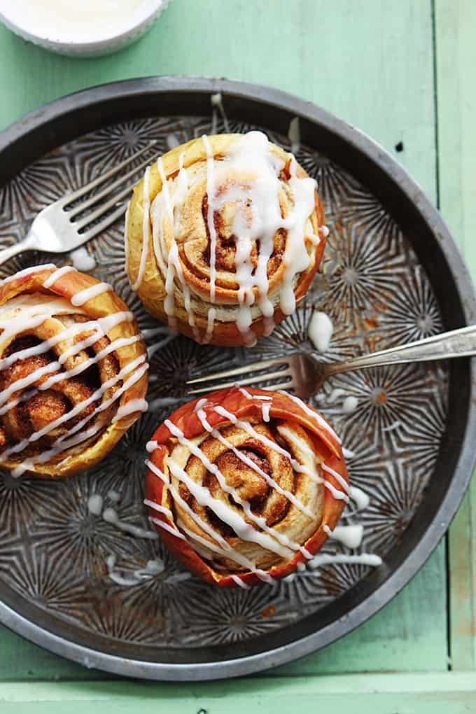 top view of cinnamon roll stuffed baked apples topped with cream cheese frosting with forks on the side all on a serving tray.