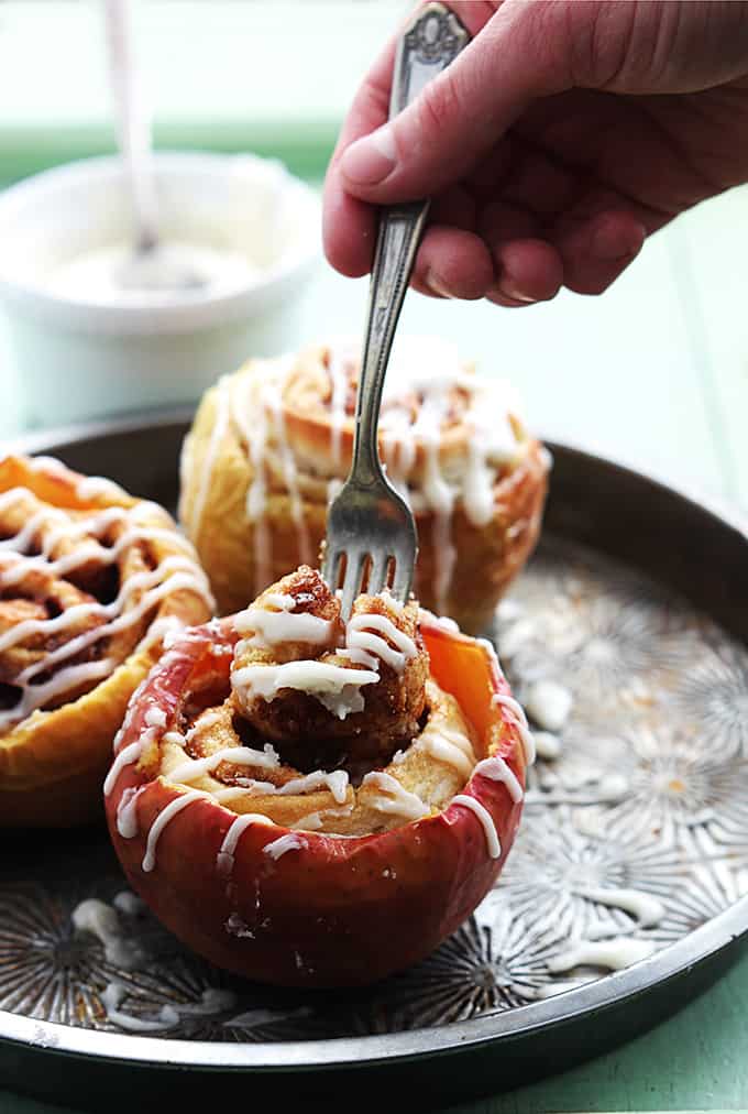 a hand taking a bite of cinnamon roll out of a cinnamon roll stuffed baked apple with more stuffed apples in the background.