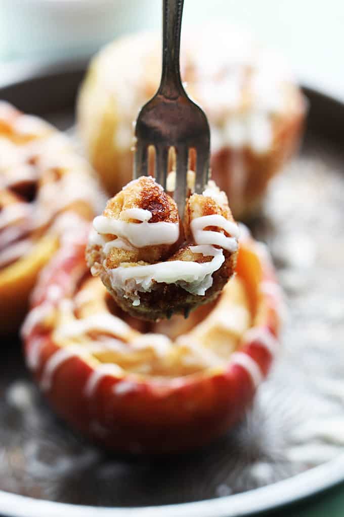 close up of a fork with a bite of cinnamon roll on it with cinnamon roll stuffed baked apples faded in the background.