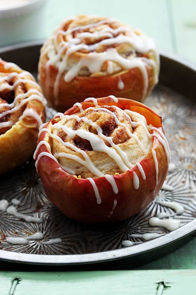 cinnamon roll stuffed baked apples topped with cream cheese frosting on a serving tray.