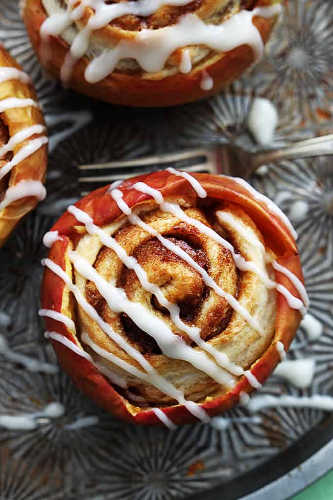 top view of a cinnamon roll stuffed baked apple topped with cream cheese frosting with a fork and more stuffed apples on the side.