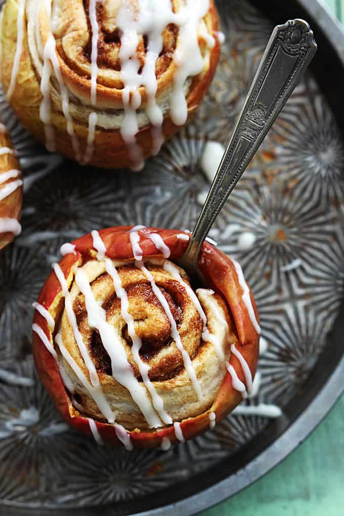 Citop view of a cinnamon roll stuffed baked apples with a fork inside the apple with more stuffed apples on the side.