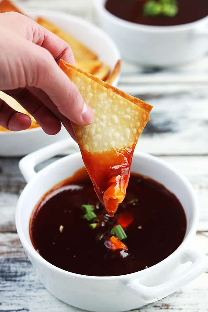 a hand holding a wonton dipped in cream cheese wonton dip above a bowl full of dip.