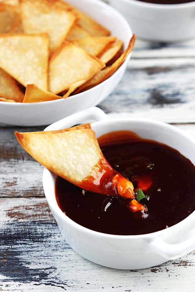 a wonton dipped in cream cheese wonton dip sitting on top of a bowl of dip with a bowl of wontons on the side.