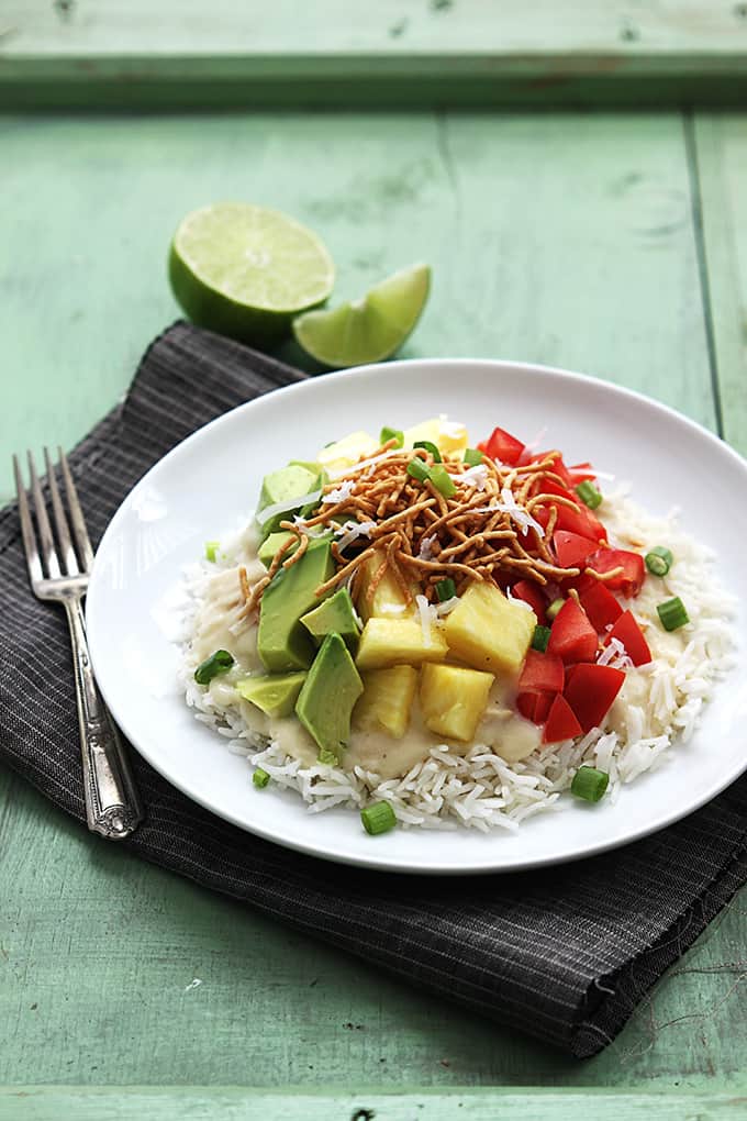 slow cooker Hawaiian haystacks on a plate with a fork and limes on the side all on a cloth napkin.