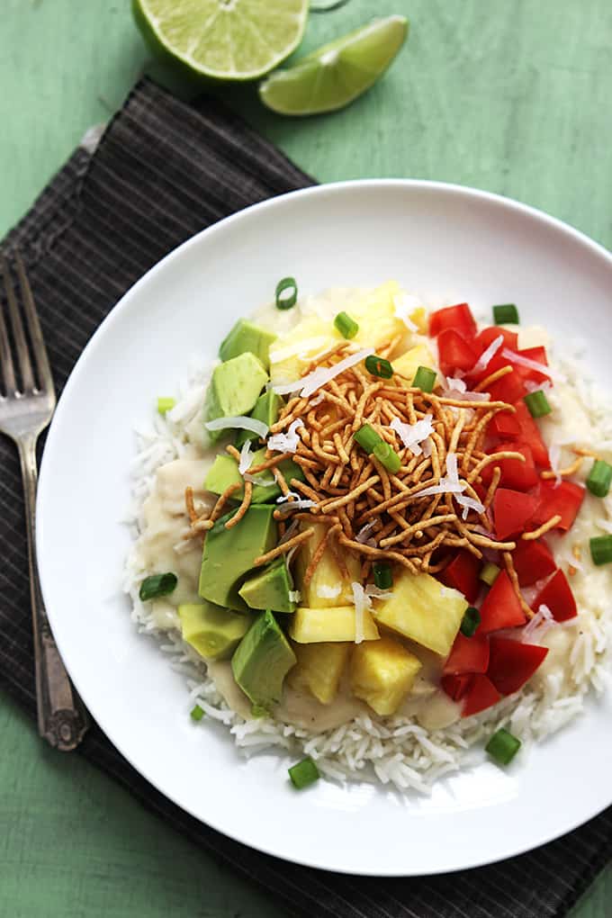 top view of slow cooker Hawaiian haystacks on a plate with a fork and a slice and a half of a lime on the side all on a cloth napkin.