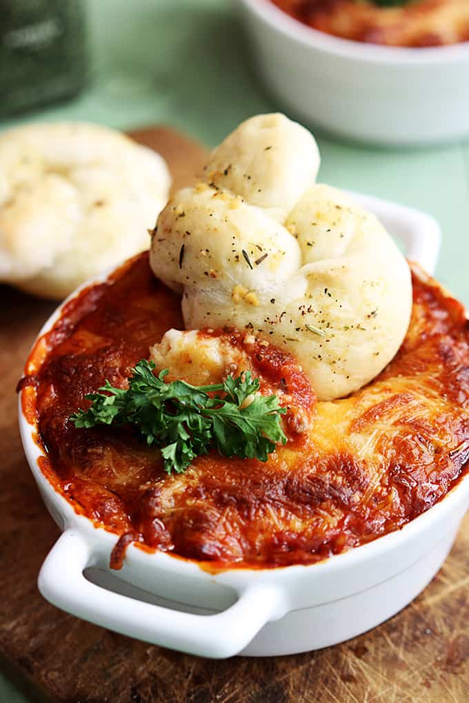 lasagna dip in a serving bowl with a breaded knot on top with another knot and more dip faded in the background.