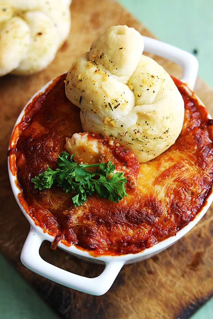 close up top view of lasagna dip in a serving bowl with a breaded knot dipped in it.