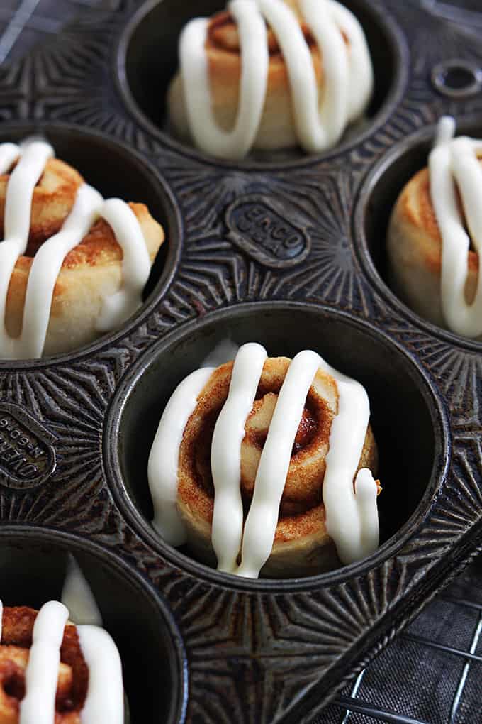 mini cinnamon rolls topped with cream cheese frosting in a muffin tin.