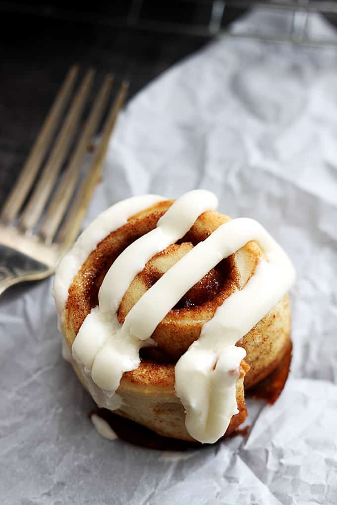 a mini cinnamon roll topped with cream cheese frosting with a fork on the side.