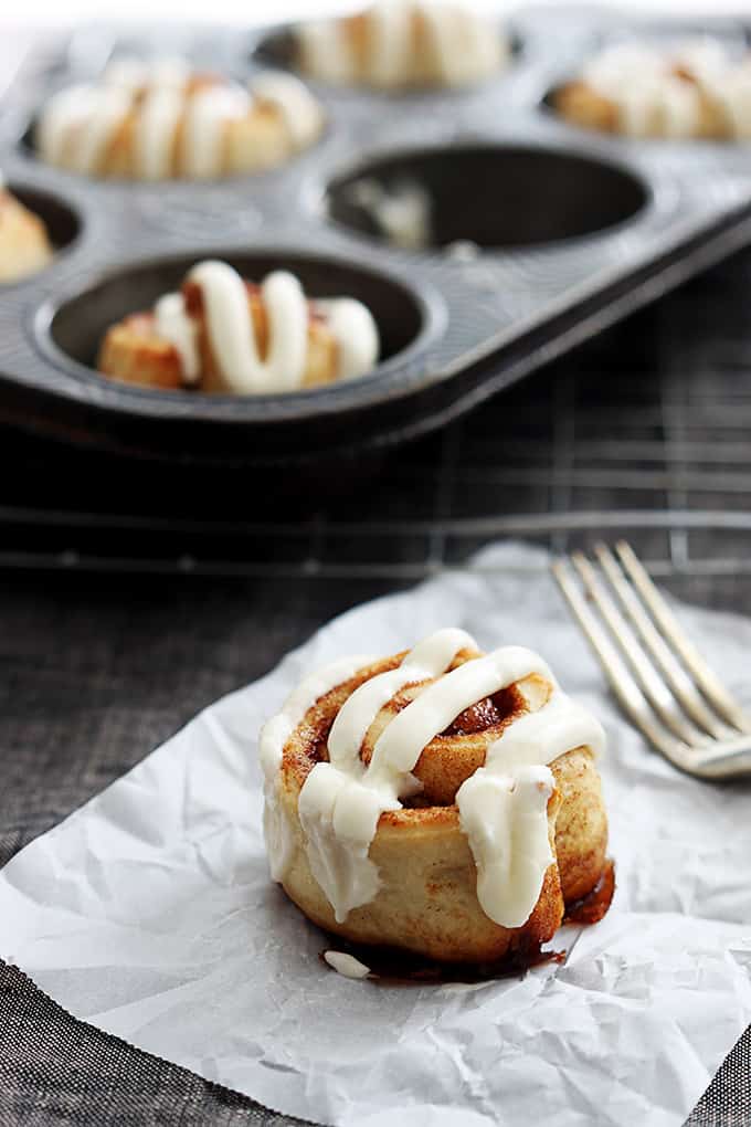 a mini cinnamon roll with a for on the side with a muffin tin with more rolls in the background.