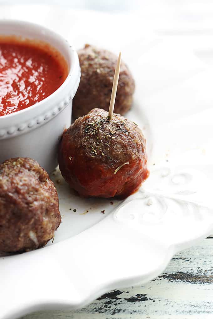 slow cooker mozzarella stuffed meatballs around a bowl of marinara sauce with the middle meatball having sauce on it.