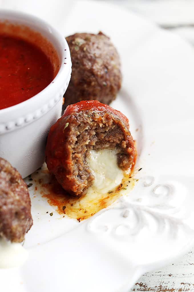 slow cooker mozzarella stuffed meatballs around a bowl of marinara sauce with a bite taken out of the middle one.