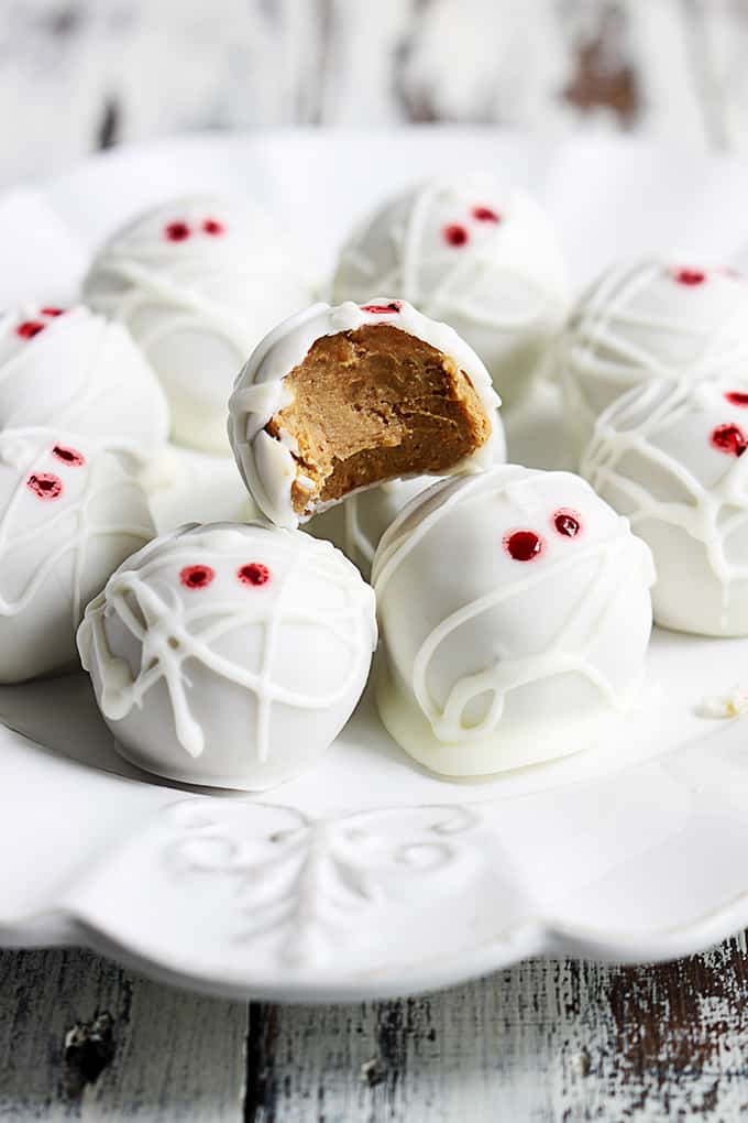 pumpkin cheesecake truffle mummies on a plate with one missing a bite.