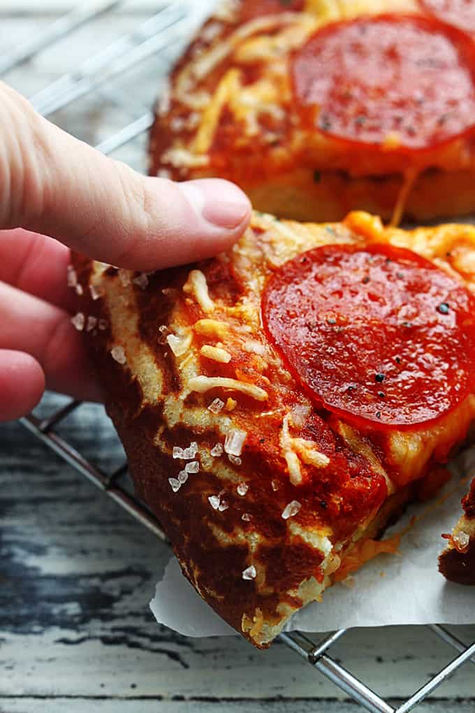 a hand taking a slice of pretzel crust pizza on a cooling rack.