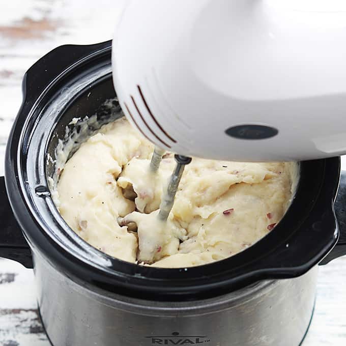 slow cooker mashed potatoes in a slow cooker being mixed with a hand mixer.