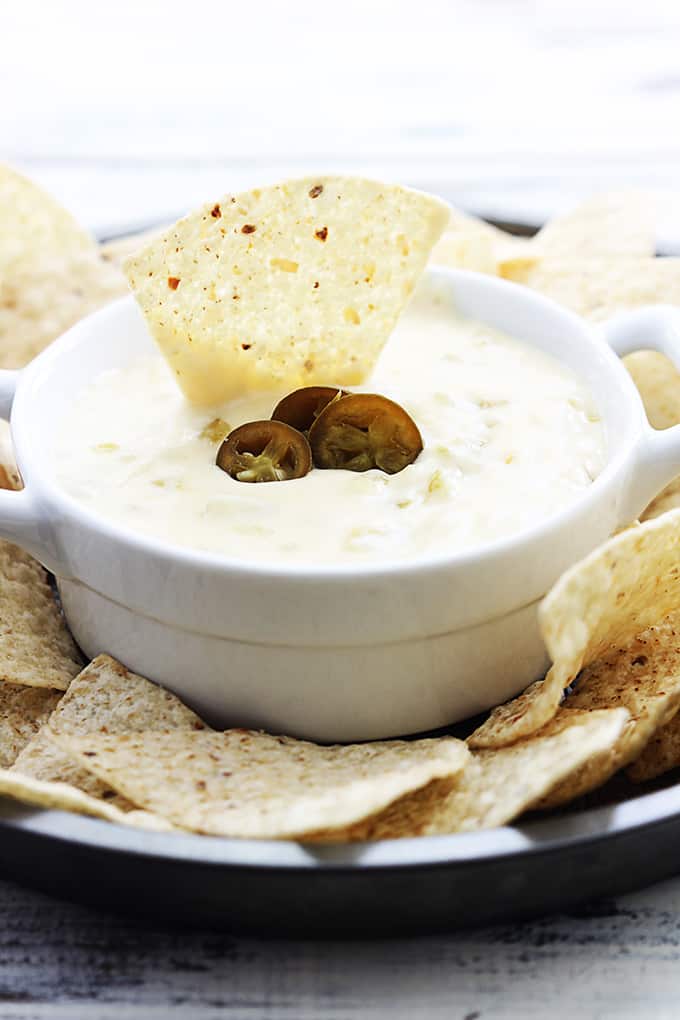 slow cooker queso blanco in a bowl with a chip dipped on top with more chips around it on a plate.