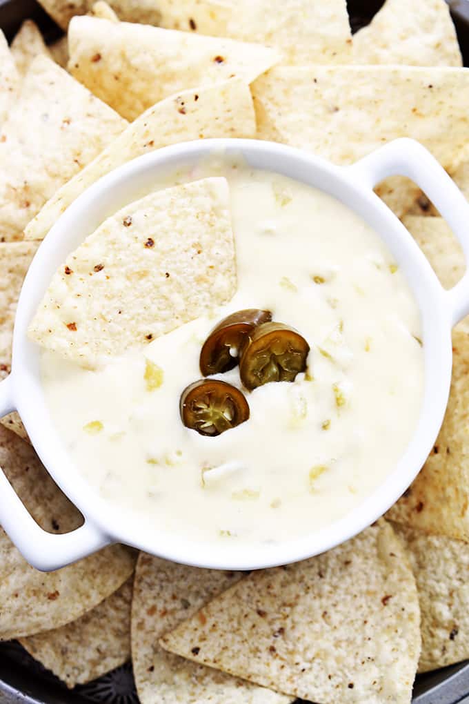 top view of slow cooker queso blanco in a bowl with a chip dipped on top with more chips around it.