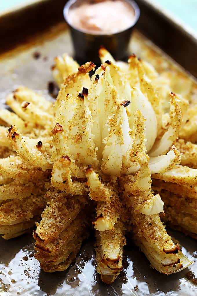 baked blooming onion on a baking sheet with dipping sauce in a small bowl on the side.