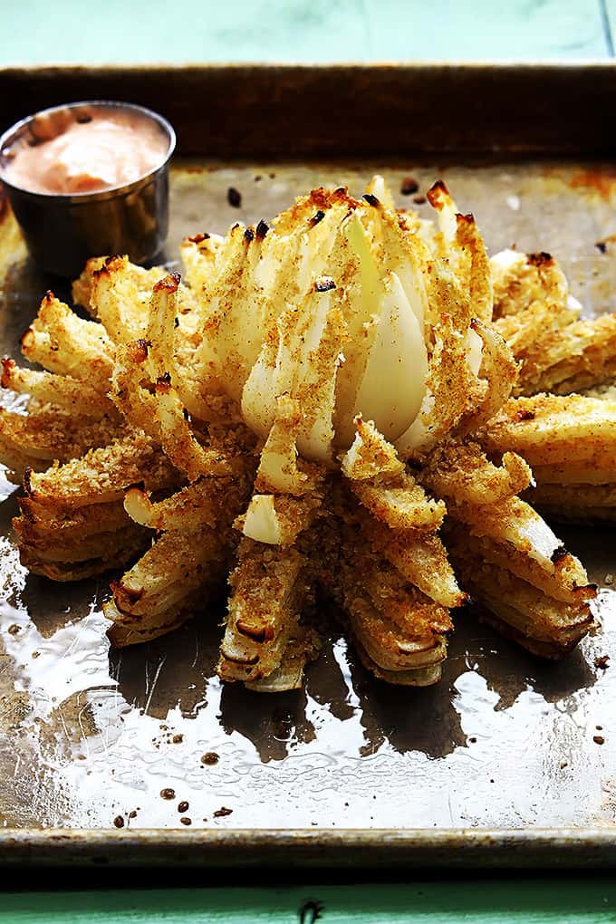 baked blooming onion on a baking sheet with a dipping bowl of sauce on the side.