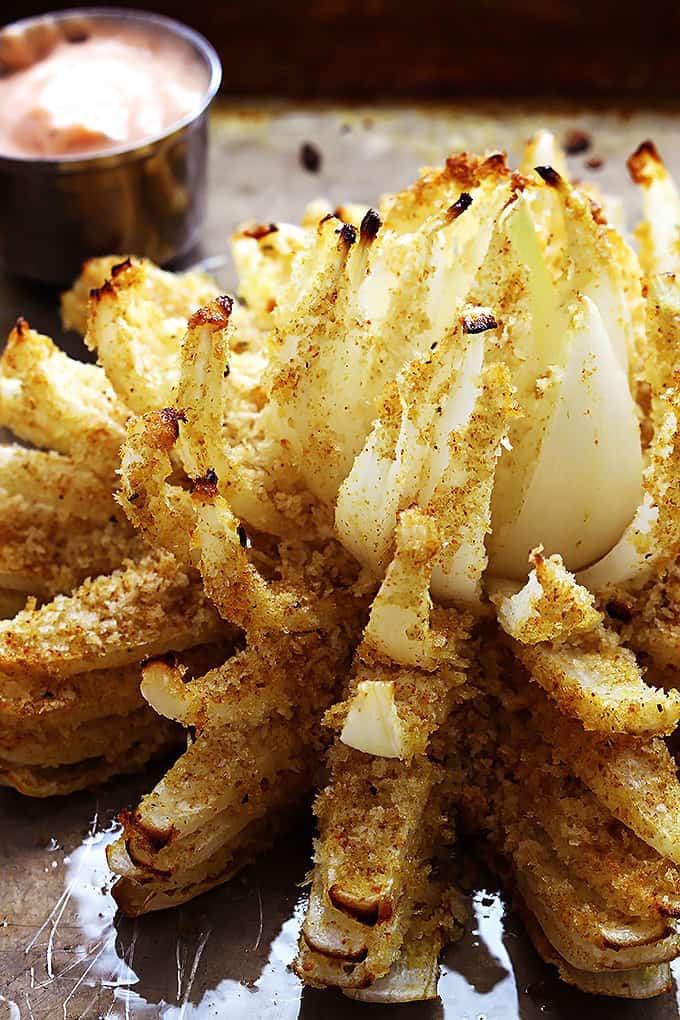 close up of baked blooming onion with a dipping bowl of sauce on the side all on a baking sheet.