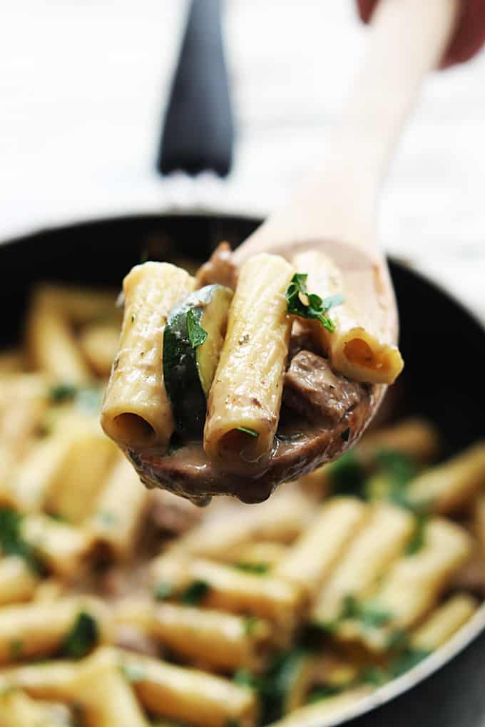 a wooden serving spoon with a scoop of speedy sausage rigatoni being held above a skillet with more pasta.