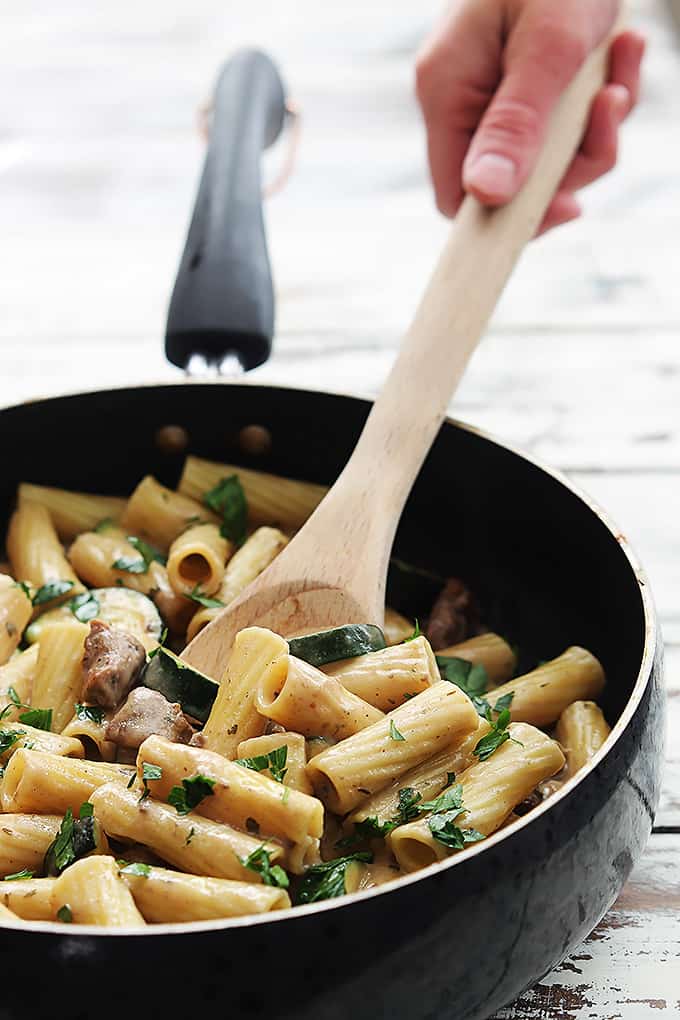 a hand scooping some speedy sausage rigatoni out of a skillet with a wooden serving spoon.