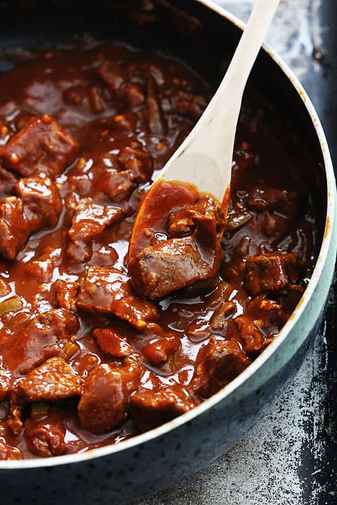 smothered Chile Colorado burrito filling in a skillet with a wooden serving spoon.