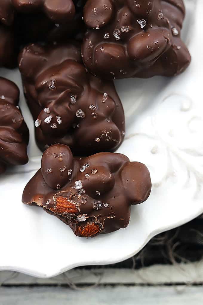 close up of chocolate almond clusters on a plate with a bite taken out of the front cluster.