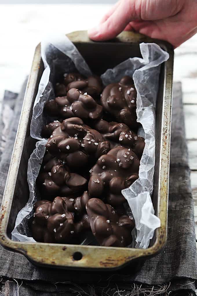 a hand holding a bread pan full of chocolate almond clusters.