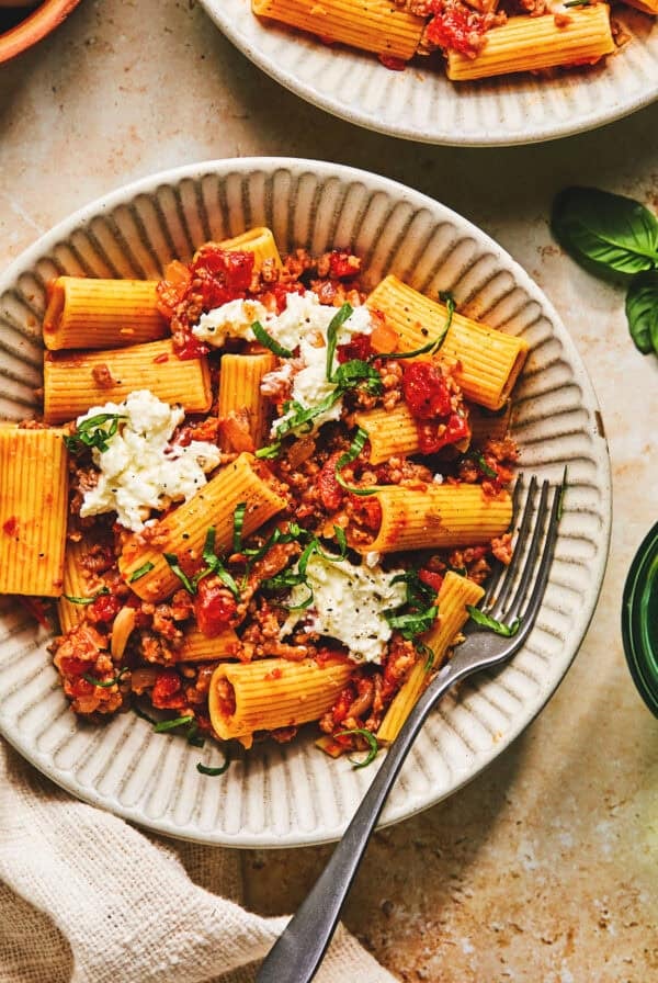 Overhead of creamy sausage pasta burrata with a fork in a white bowl.