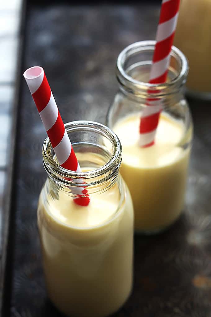 two milk jugs of eggnog with straws.