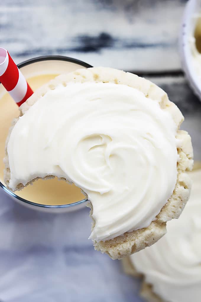 a eggnog sugar cookie with a bite taken out of it sitting on top of a glass of eggnog.